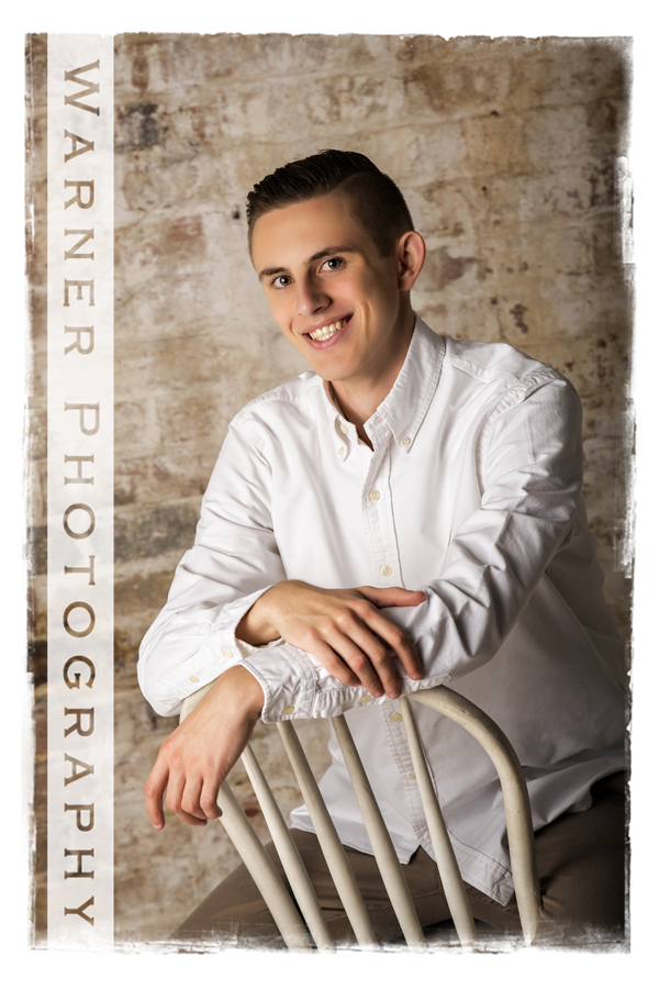 Stuio senior portrait of Dow High School senior Joey sitting on a chair in front of a brick wall