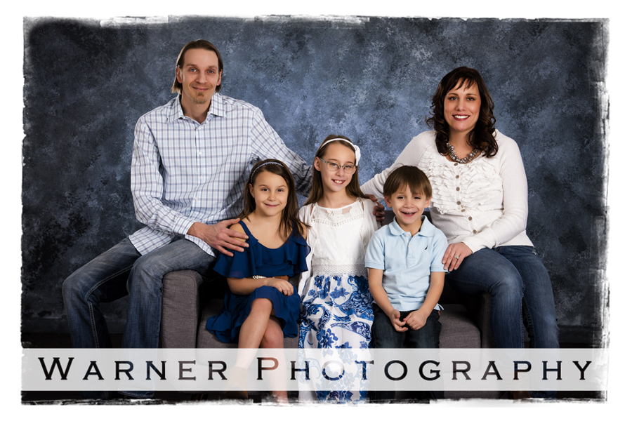 family portrait Losey family Warner Photography Studio seated on a grey couch with blue backgrounds
