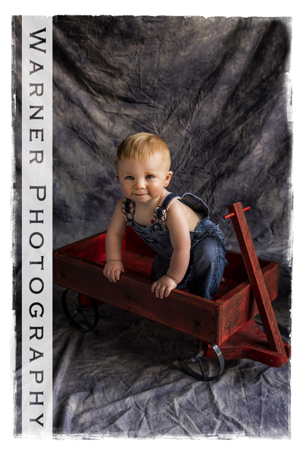 Studio childrens portrait of Wyatt in bib overals in a red wagon