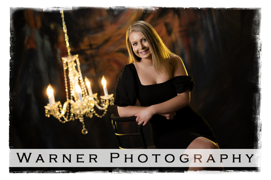 Studio senior portrait of Kayla with dark colors and a crystal chandelier