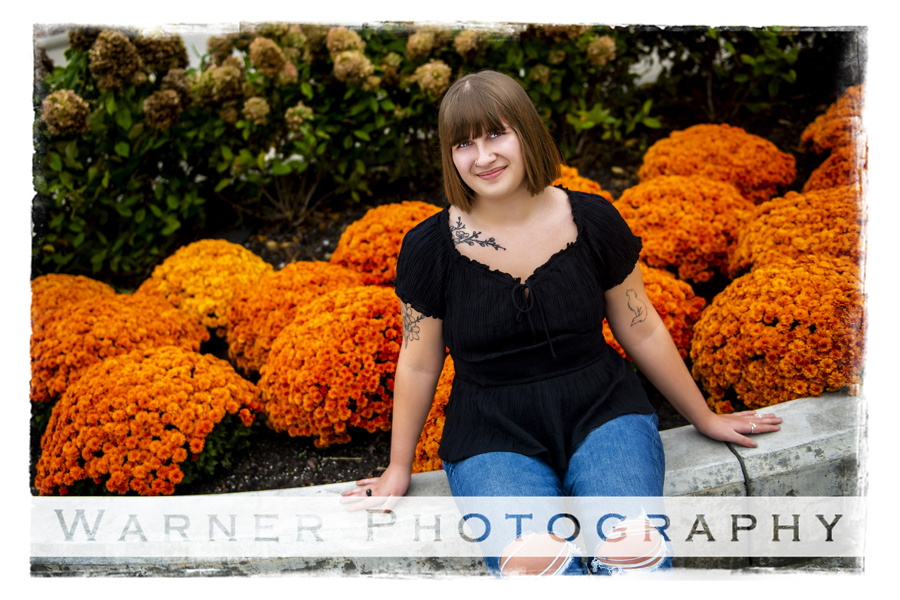 an outdoor portrait of Ogemaw Heights High School senior Cassiday at Chippewa Nature Center with orange mums